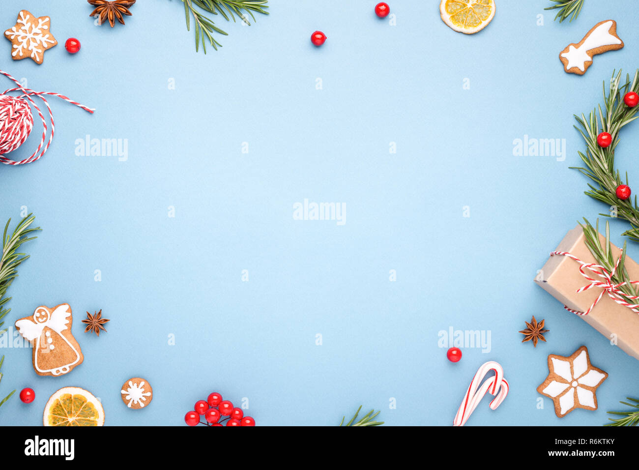 Blue Christmas background made of gigerbread cookies, rosemary branches, berries, gift box, Christmas wreath, cande cane lollipops and rope. Top view. Stock Photo