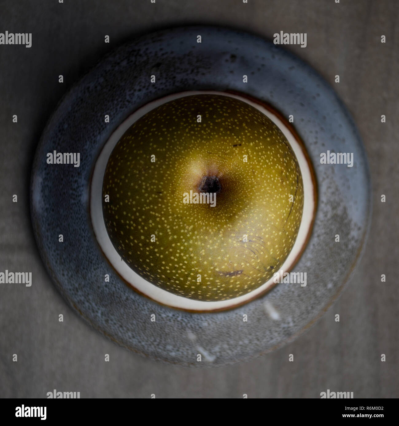 A whole Asian pear (Pyrus pyrifolia) on a small plate, shot from overhead (flat-lay). Stock Photo