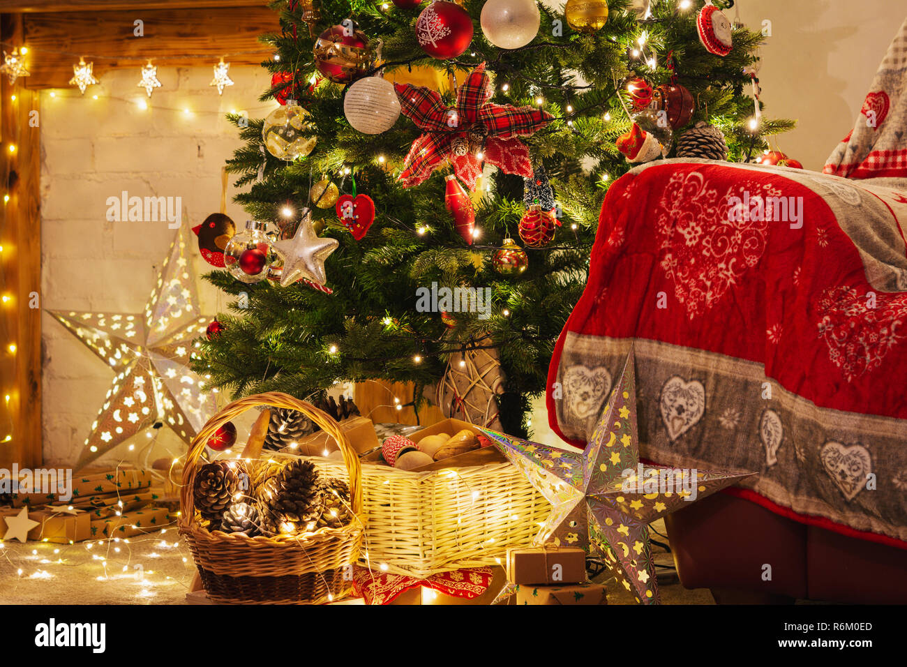 Christmas living room, decorated fireplace with wood mantelpiece, lit up Christmas tree with baubles, stars, pine cones, cosy armchair with read throw Stock Photo