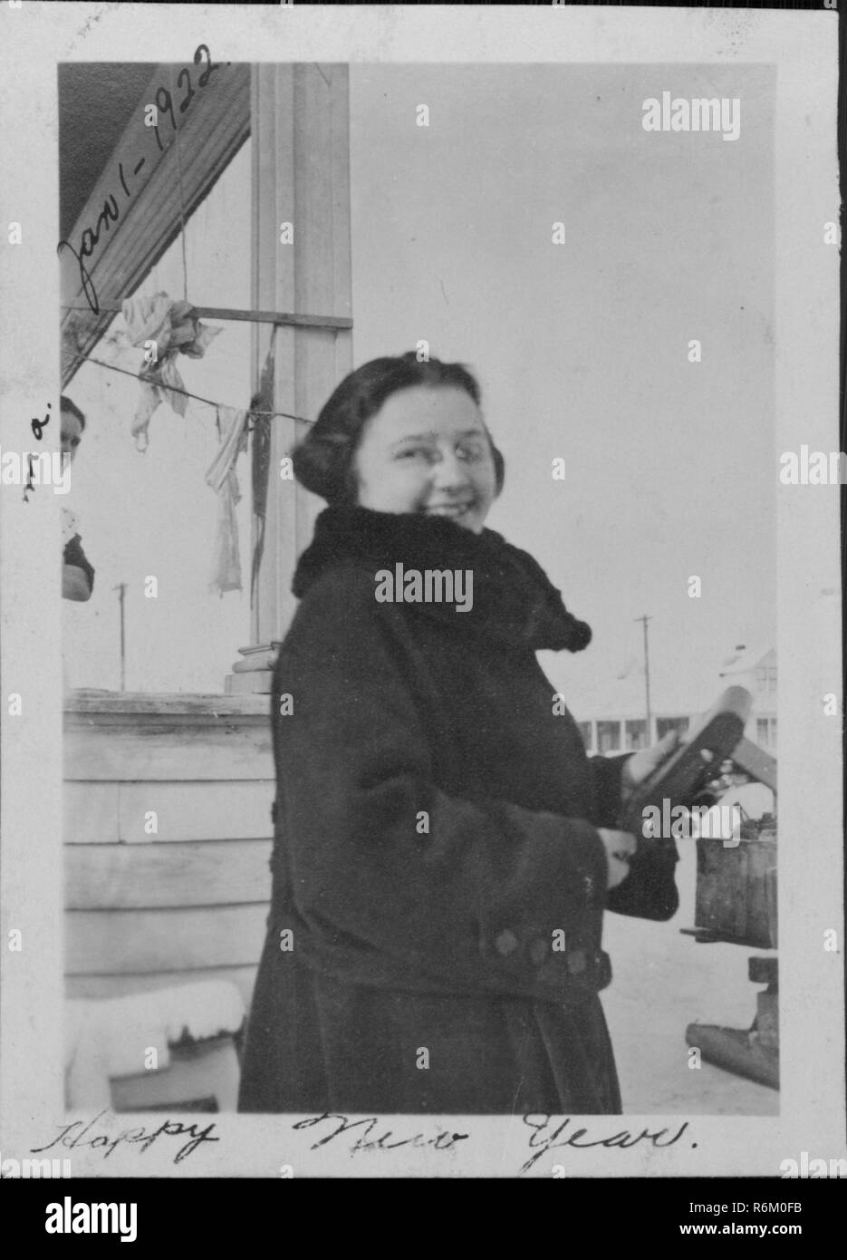 Young woman smiling and looking over her shoulder on New Year's Day while holding a medium format folding camera, 1922. () Stock Photo