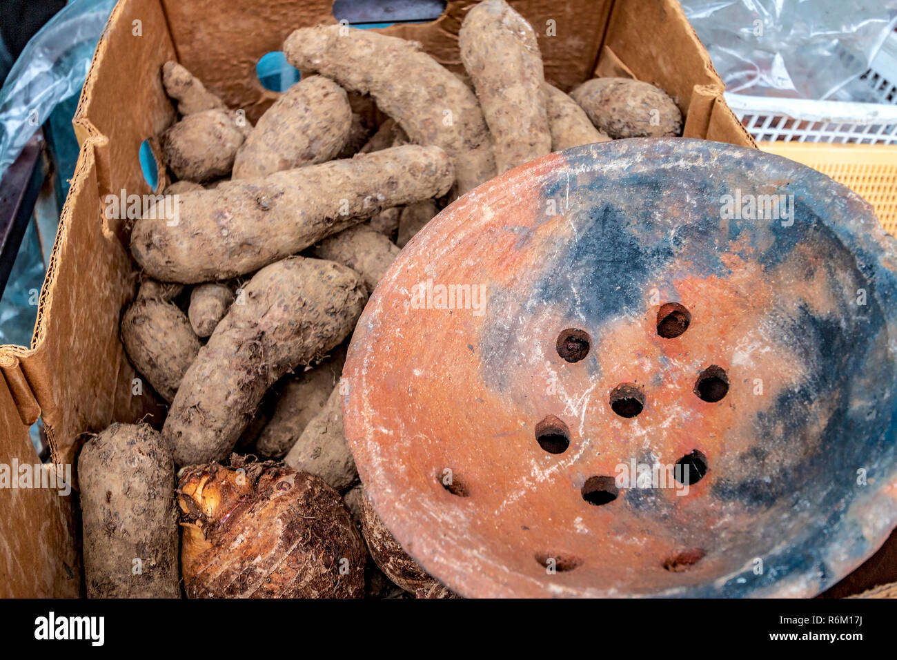 Yams and a dasheen, another root vegetable, for sale along a street in Bridgetown, Barbados. The clay dish is part of a coal pot, an old cooking tool carried over from colonial and Carib Indian culture. Stock Photo