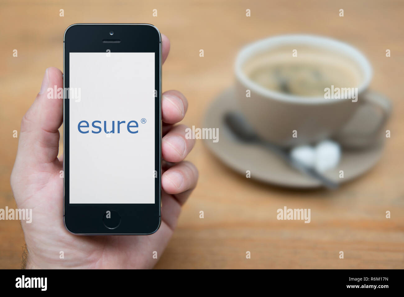 A man looks at his iPhone which displays the esure logo (Editorial use