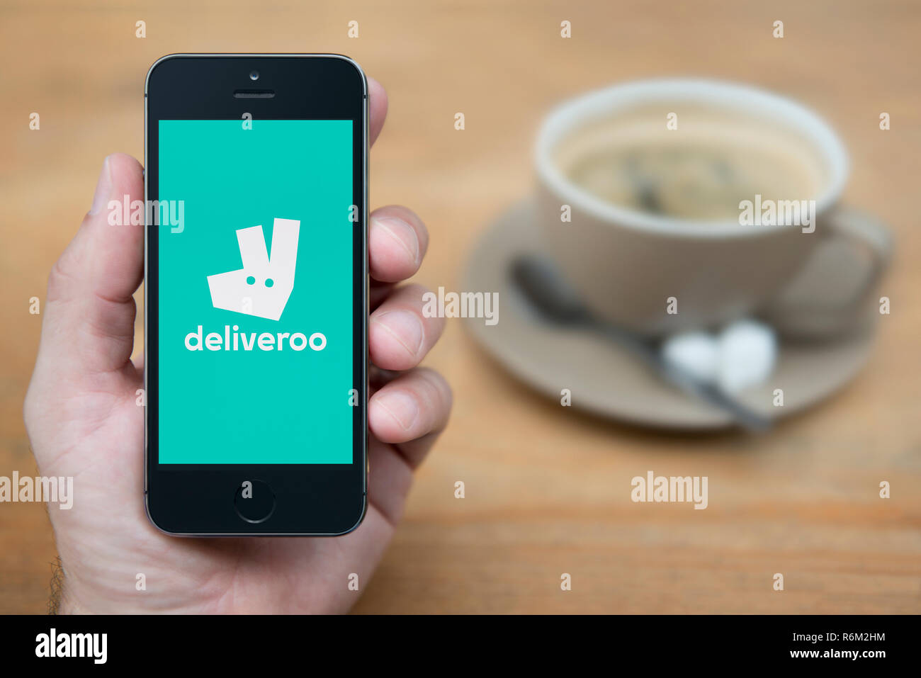 A man looks at his iPhone which displays the Deliveroo logo (Editorial use only). Stock Photo