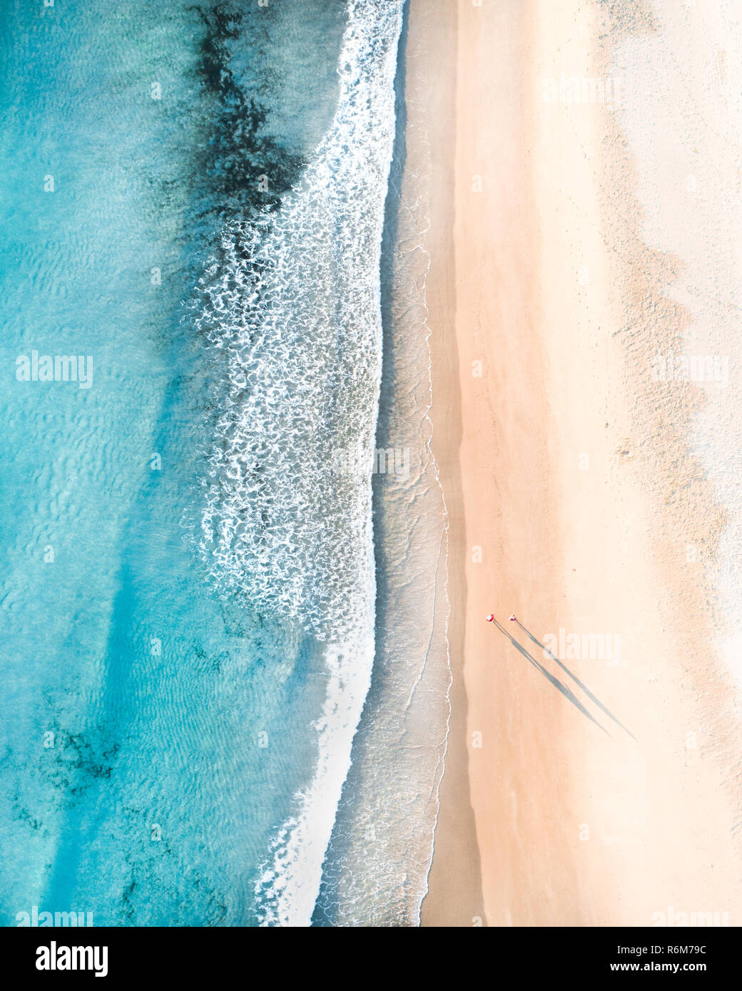 Aerial of people walking on a beach at sunrise with  beautiful sand beach and gentle waves Stock Photo