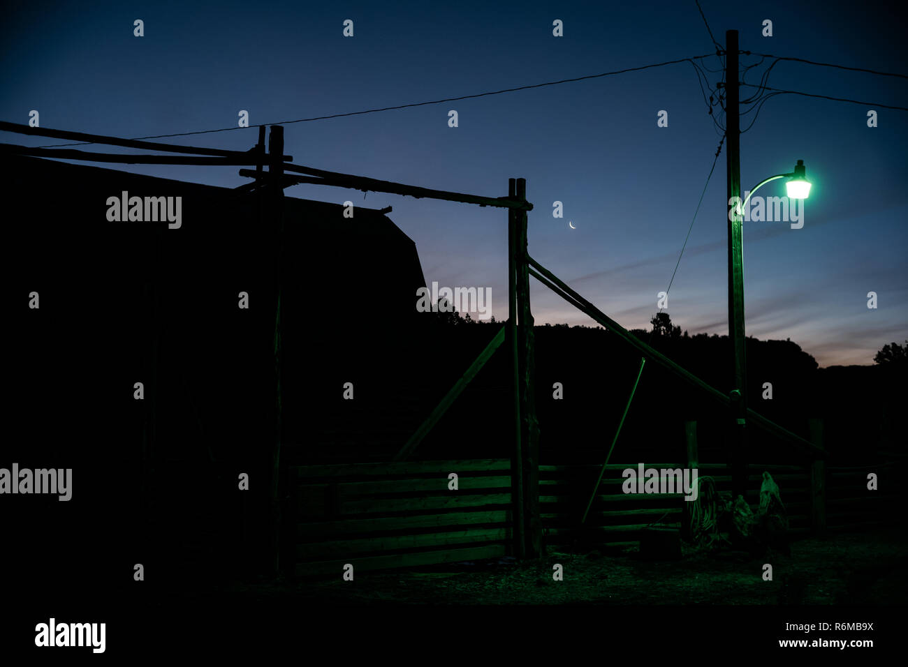 Ranch barn during sunrise sunset with moon in background and fluorescent light in foreground. Stock Photo