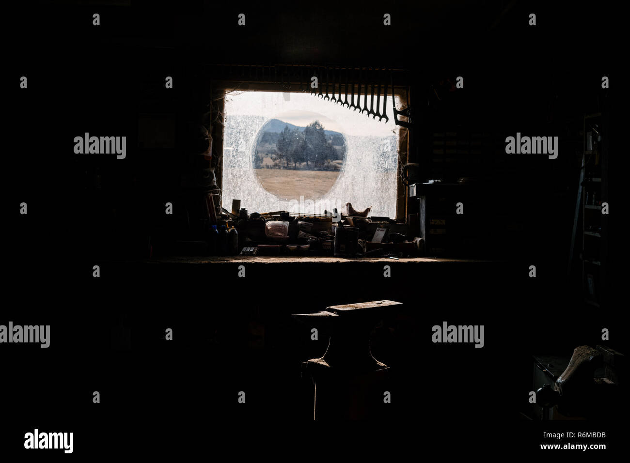 Neatly organized seasoned wrenches farm tools hang next to a dirty sunlit window in an old barn on a ranch. Stock Photo