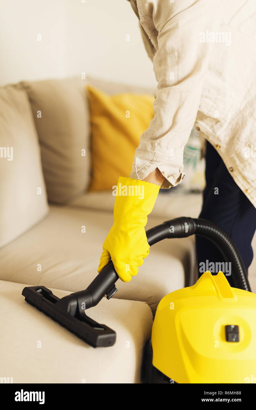 Woman cleaning sofa with yellow vacuum cleaner. Copy space. Clean