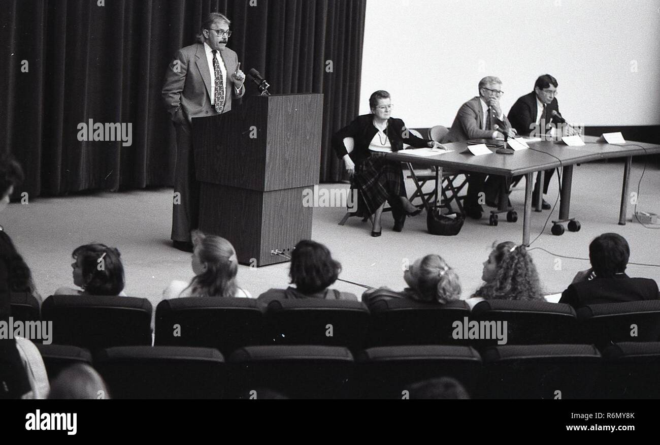 A MAN STANDING AT THE PODIUM GIVING A SPEECH WITH TWO OTHER PEOPLE ON ...