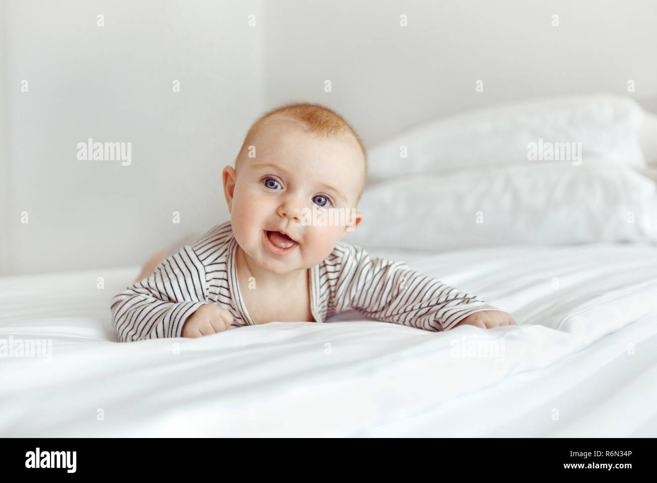 Charming happy baby on white bed Stock Photo