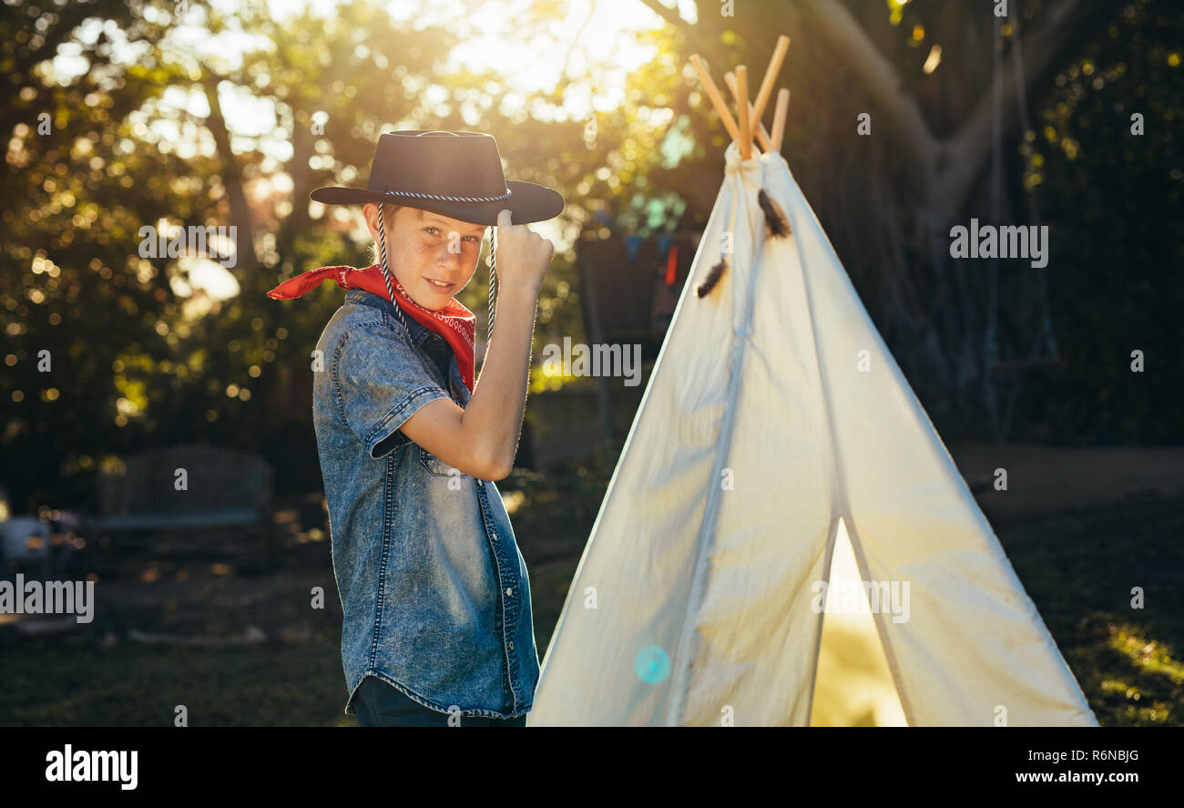 Portrait of young boy posing in cowboy hat by a backyard garden teepee. Little boy having fun in the backyard outdoors. Stock Photo