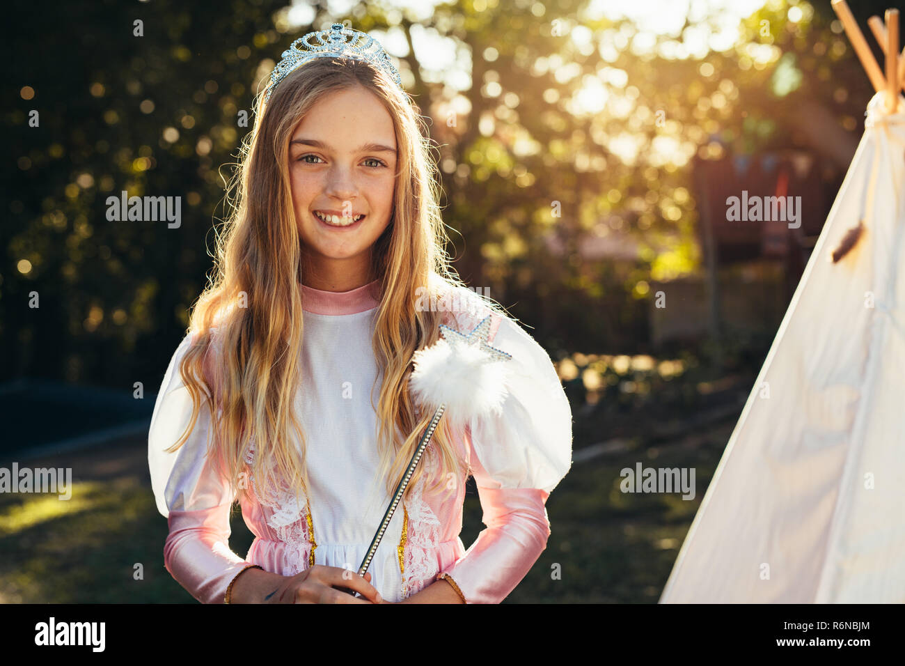 Beautiful little girl in fairy costume wearing crown and holding wand.  Cute young girl in fairy costume playing in garden. Stock Photo