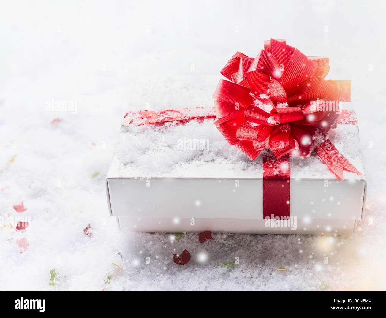 White gift box with red bow on snow with bokeh and snowfall. Copy space ...