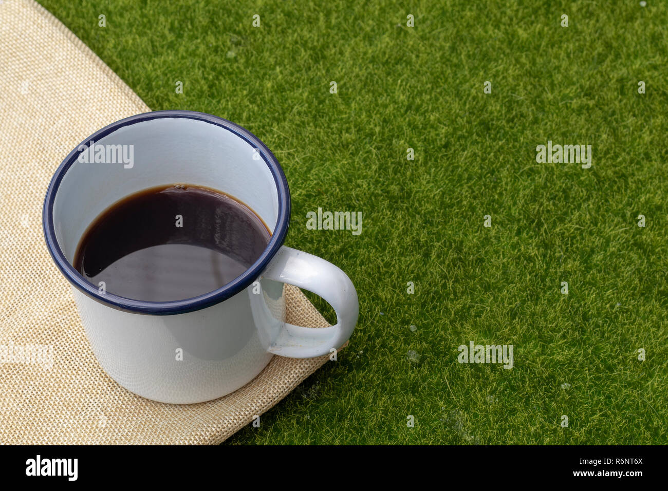 Coffee in white tin cup on grass background. Stock Photo