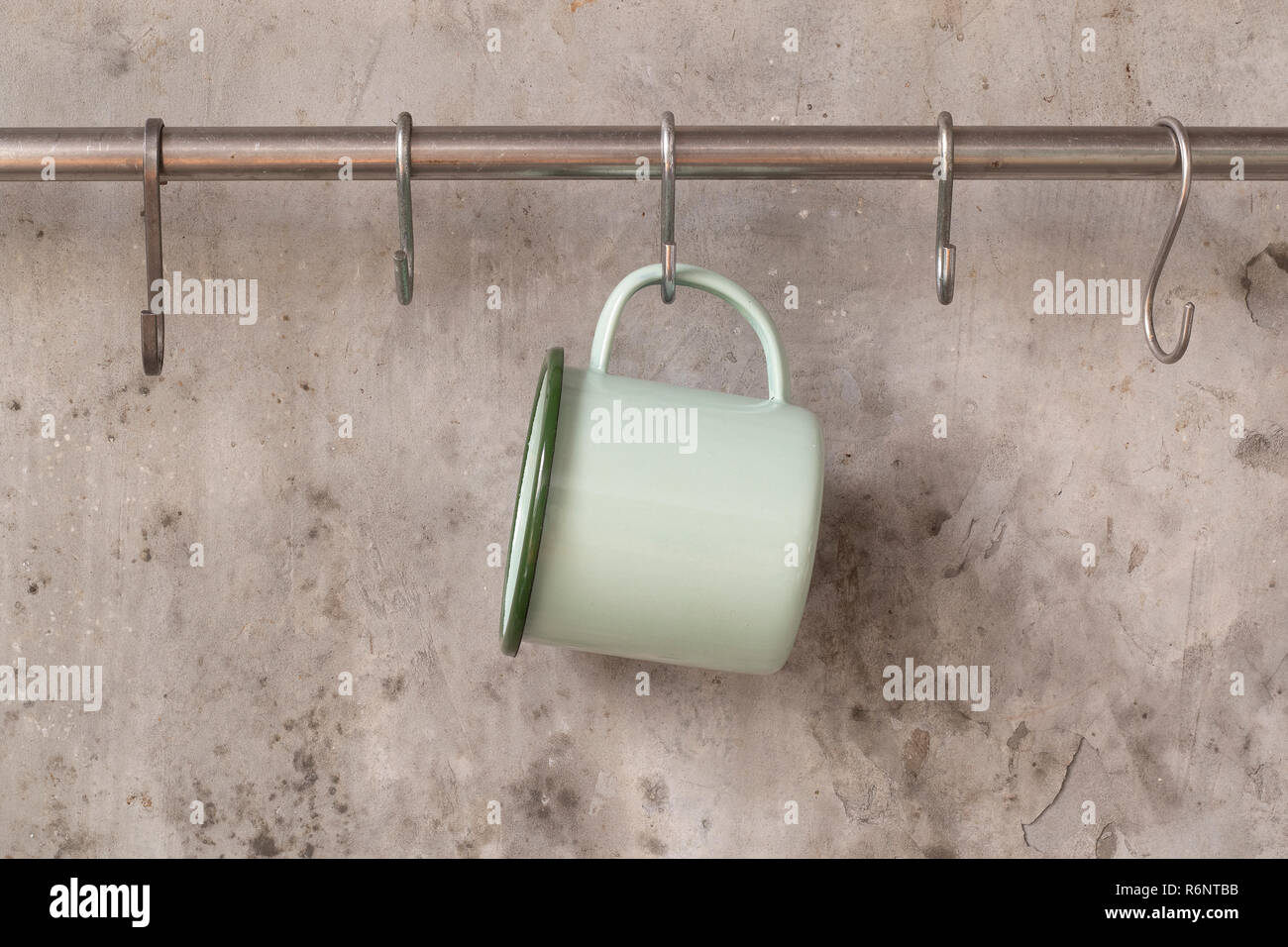 Green tin cup hanging on stainless rail on cement wall background Stock