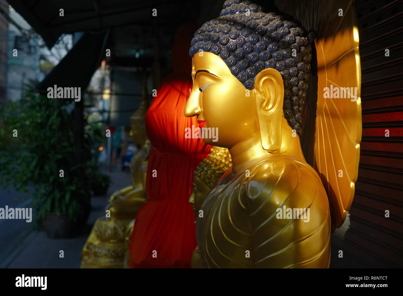 A Buddha statue outside a factory for Buddha statues in Bamrung Muang Road, Bangkok, Thailand, is illuminated by the first rays of the rising sun Stock Photo