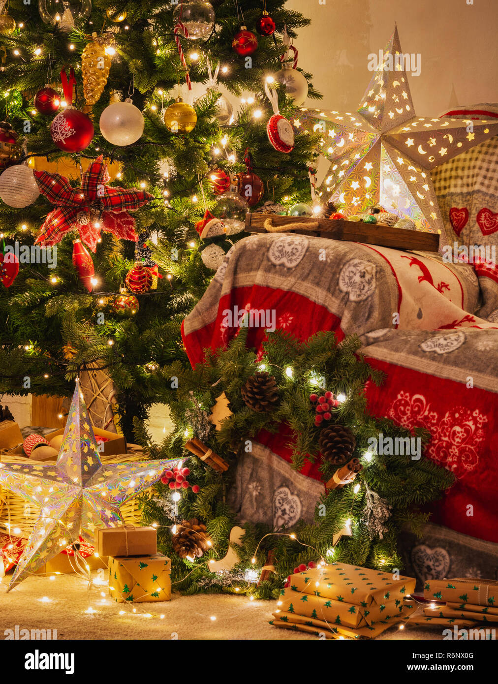 Christmas living room, decorated fireplace with wood mantelpiece, lit up Christmas tree with baubles, stars, pine cones, cosy armchair with read throw Stock Photo