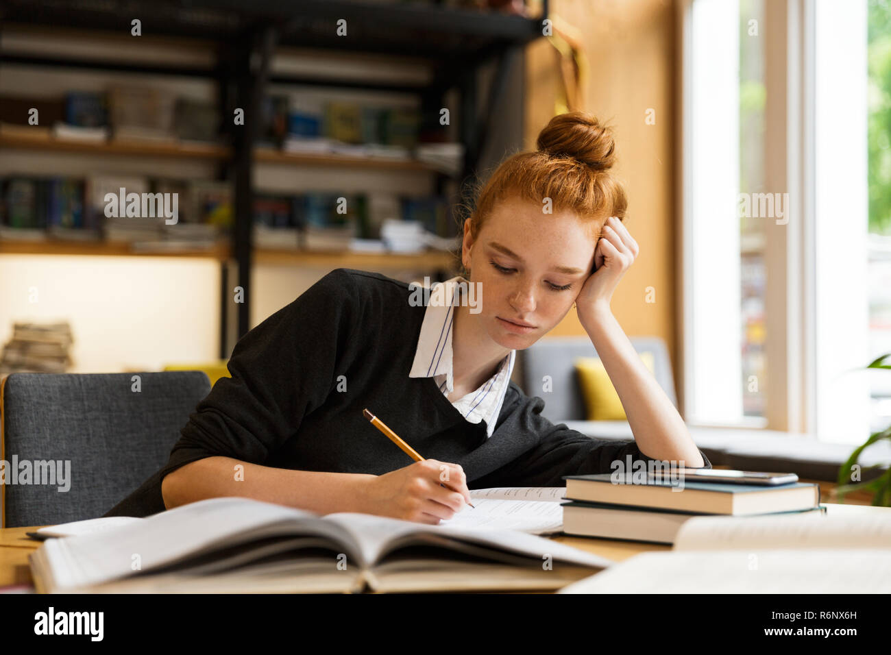Image of smart teenage girl studying while sitting at desk in college