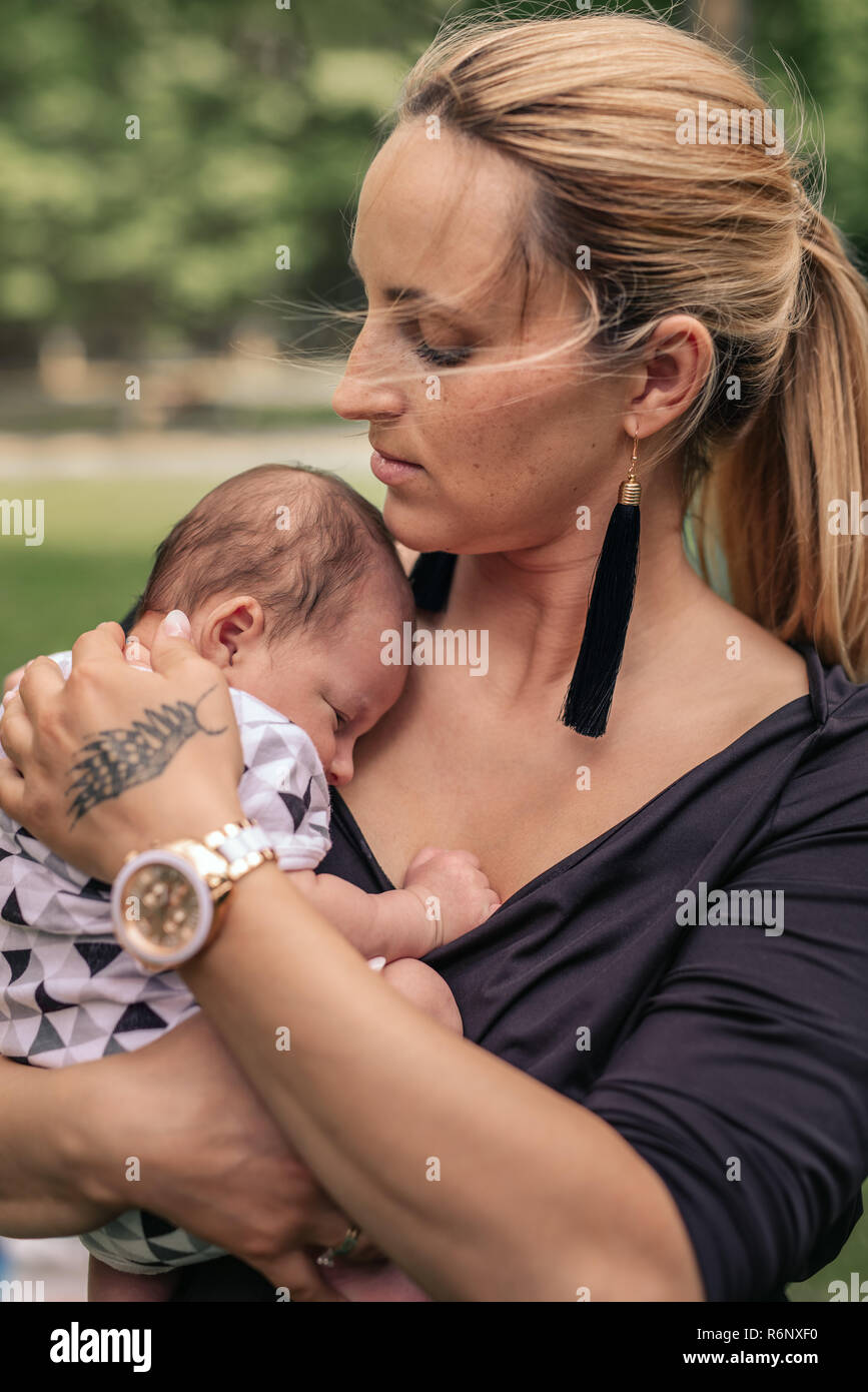 Loving mother cradling her baby boy on her shoulder outside Stock Photo