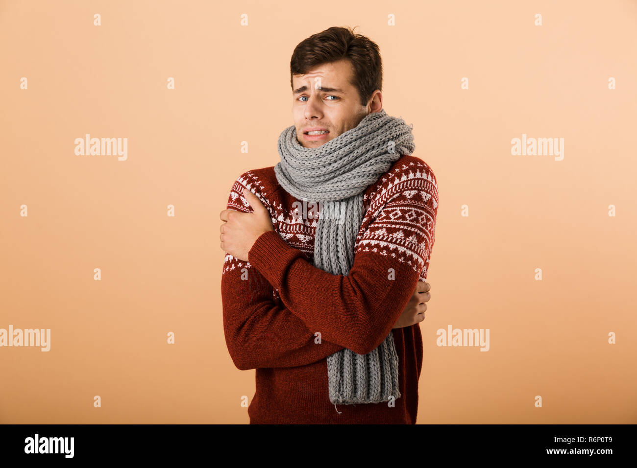 Portrait a young man dressed in sweater and scarf isolated over beige background, shaking Stock Photo