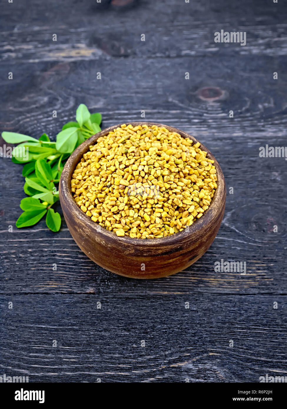 Fenugreek with green leaf in clay bowl on wooden board Stock Photo
