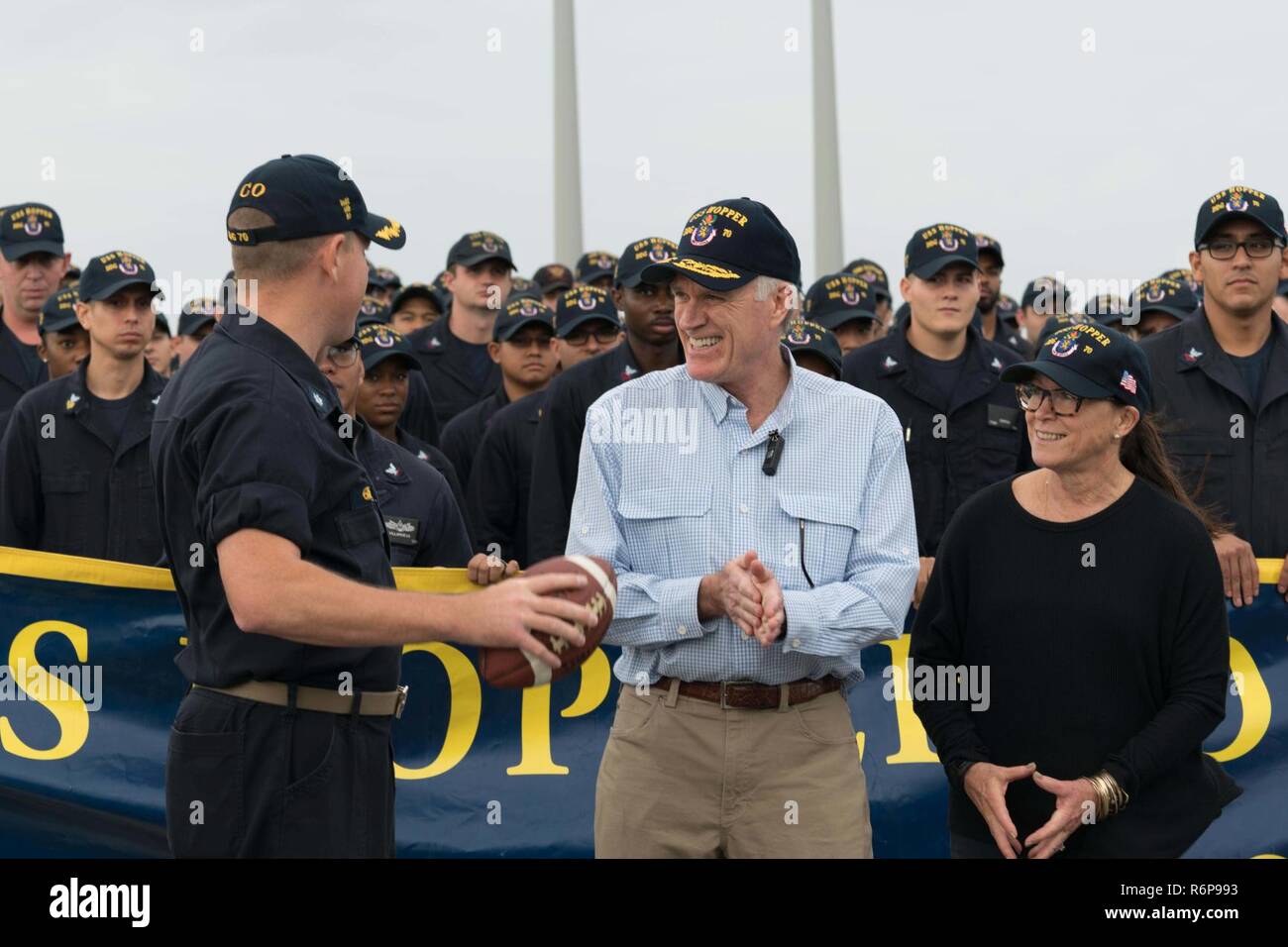 ARABIAN GULF (Nov. 23, 2017) Cmdr. Jeffrey Tamulevich (left), commanding officer of the Arleigh Burke-class guided-missile destroyer USS Hopper (DDG 70), speaks with the Secretary of the Navy (SECNAV) Richard V. Spencer and his wife, Sarah Pauline Spencer, prior to the filming of a spirit spot on the ship’s flight deck for the upcoming Navy vs. Army game, during the SECNAV’s visit to the ship on Thanksgiving Day. Hopper is deployed to the U.S. 5th Fleet area of operations in support of maritime security operations to reassure allies and partners and preserve the freedom of navigation and the f Stock Photo
