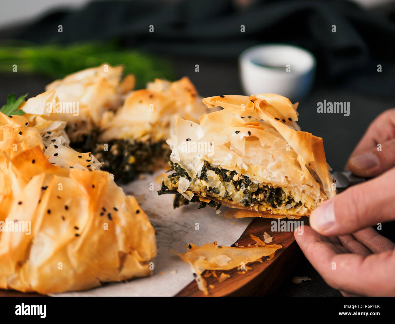 Slice of greek pie spanakopita in hand. Ideas and recipes for vegetarian or vegan Spanakopita Spinach Pie from fillo pastry cut in slices. Copy space. Side view Stock Photo