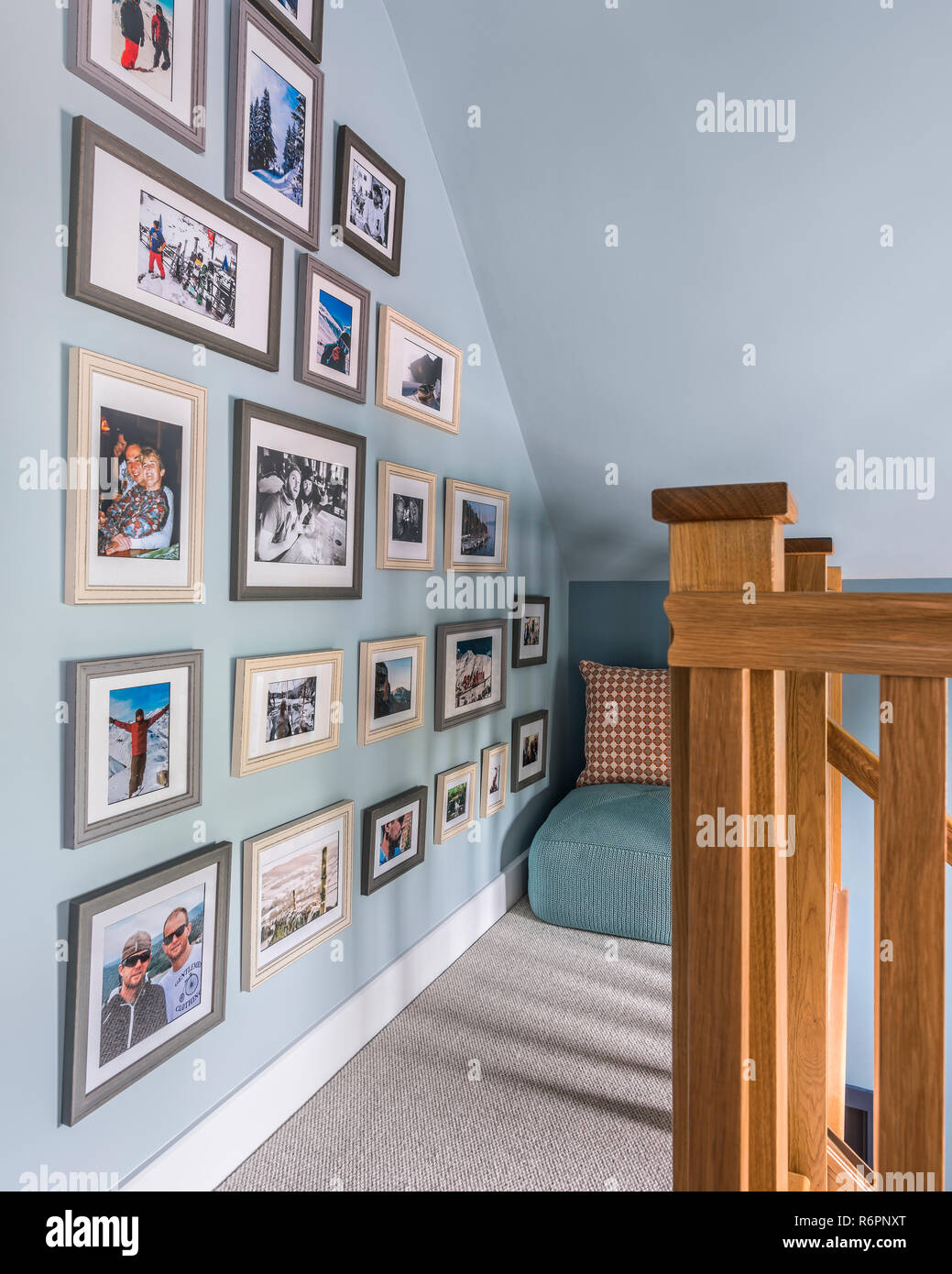 Framed family photographs on light blue wall with wooden banister in Hampshire Mill house redesigned by Emma Painter Stock Photo