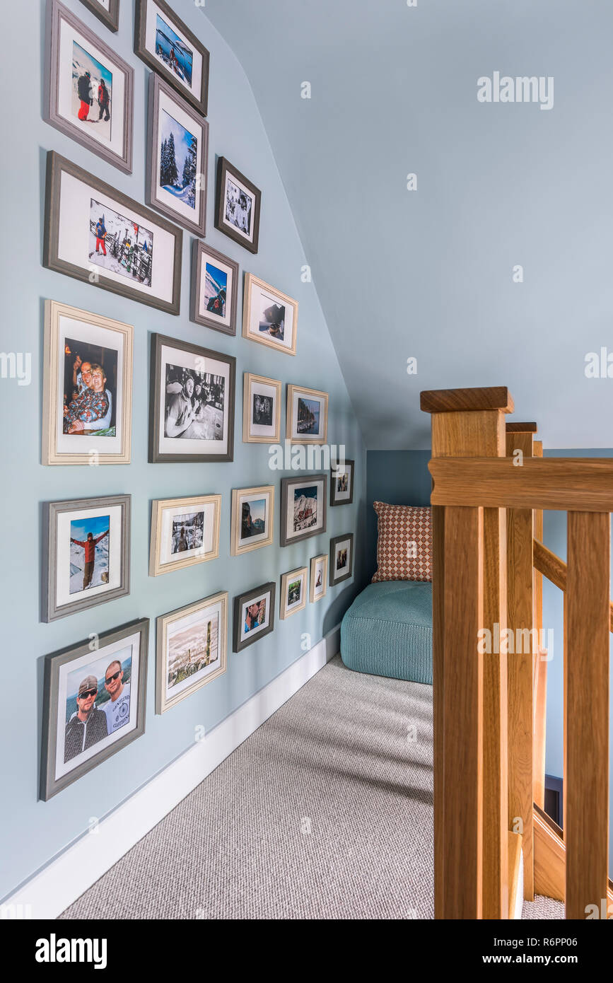 Framed family photographs on light blue wall with wooden banister in Hampshire Mill house redesigned by Emma Painter Stock Photo