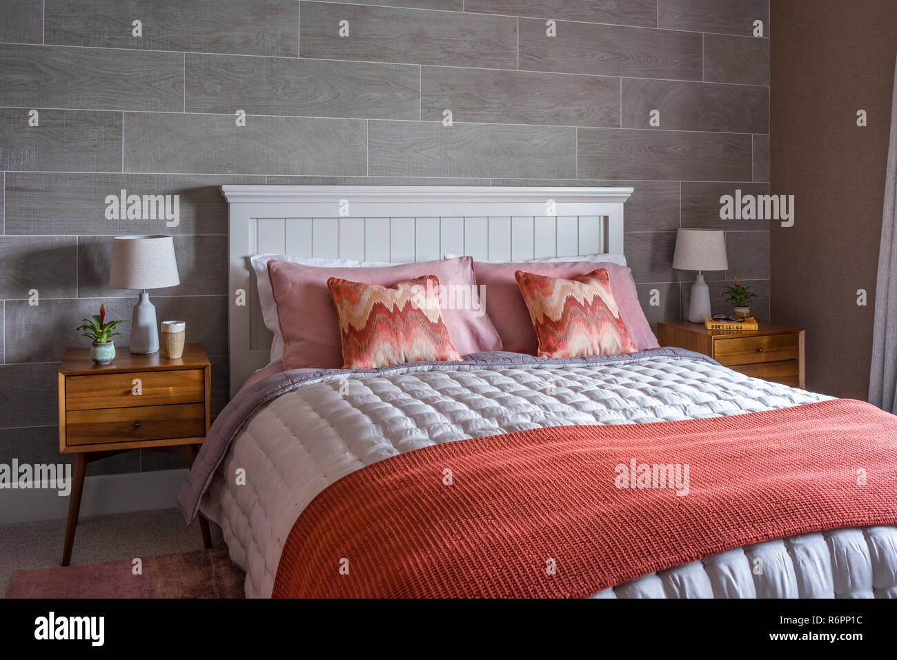 Wooden bedaside cabinet with coral pillows and blanket on double bed in  Hampshire Mill house redesigned by Emma Painter Stock Photo