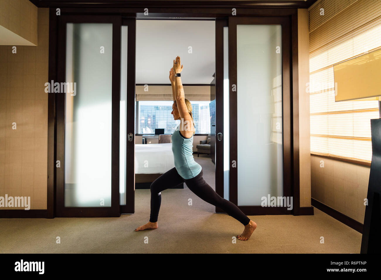 Beautiful millennial woman practicing yoga in hotel room on business travel Stock Photo
