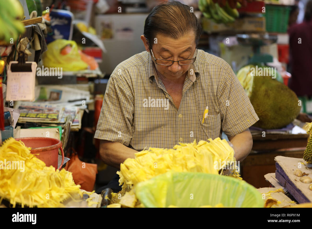 Shopkeeper of the fruit and vegetable market in Little India, Singapore, cleans the inside of the jackfruit, a large tropical fruits, for sale. Stock Photo