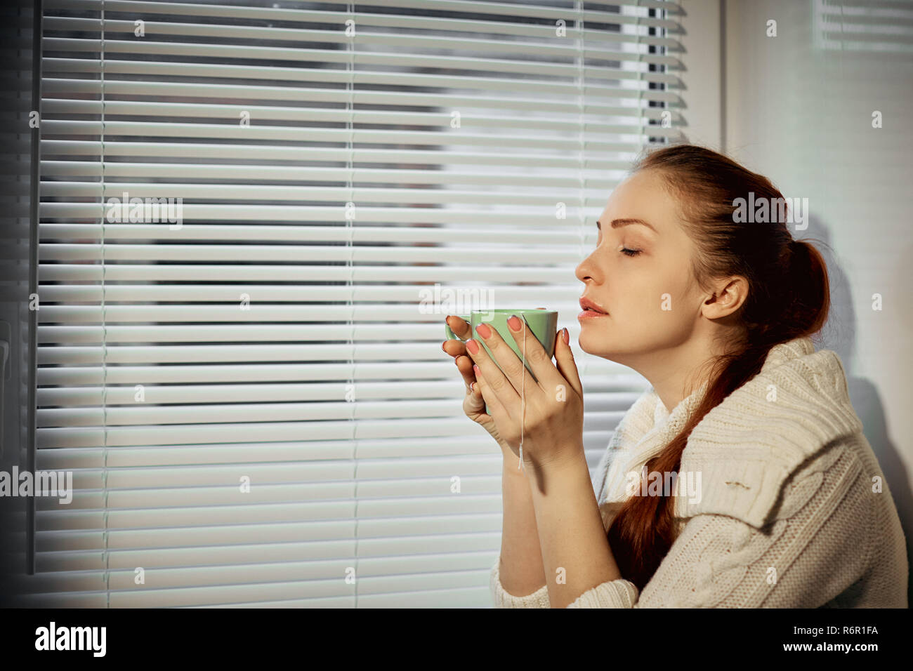 woman holding a Cup of tea and drinking sitting around the window Stock Photo