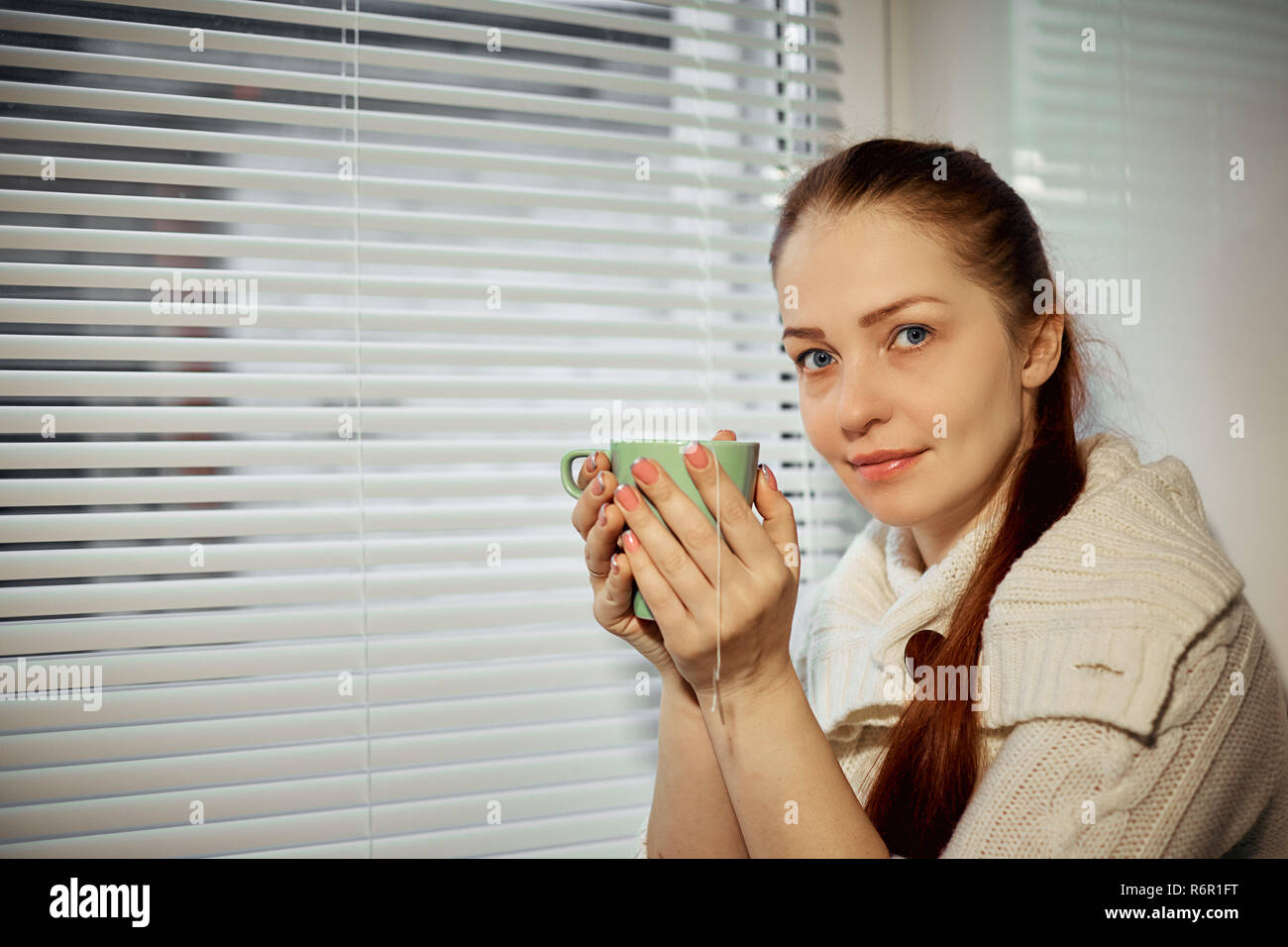woman holding a Cup of tea and drinking sitting around the window Stock Photo