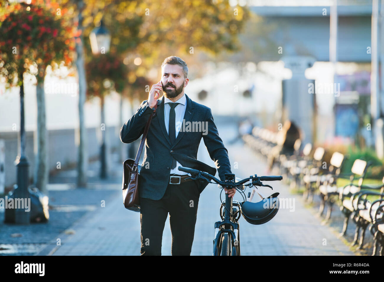 A businessman commuter with bicycle walking home from work in city, using smartphone. Stock Photo
