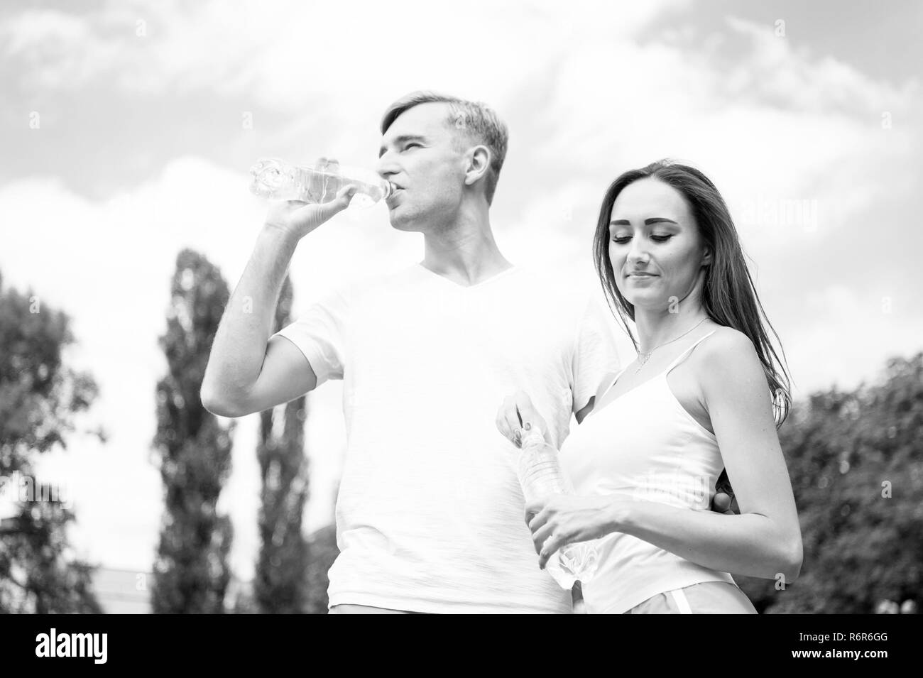 Sport and health. Summer activity and energy. Couple of coach relax after workout. Girl and guy sunny outdoor. Woman and man drink water from bottle. Stock Photo