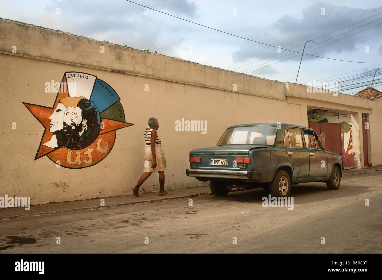 Woman walking by a wall art propaganda of the Cuban Revolution, with a typical Russian classic car. Trinidad, Cuba. Stock Photo