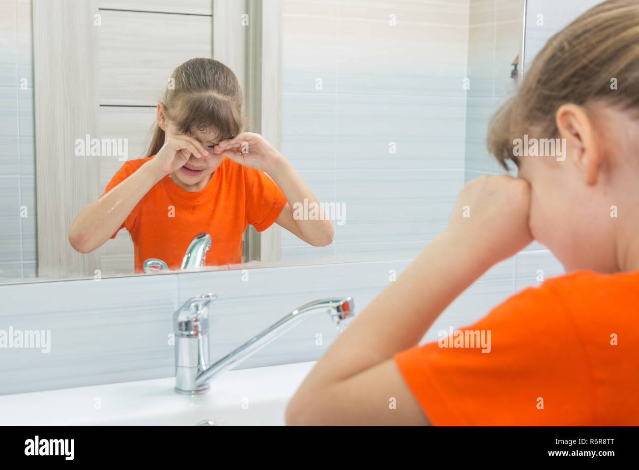 Sevenyearold girl rubs her eyes trying to wake up, washing in the