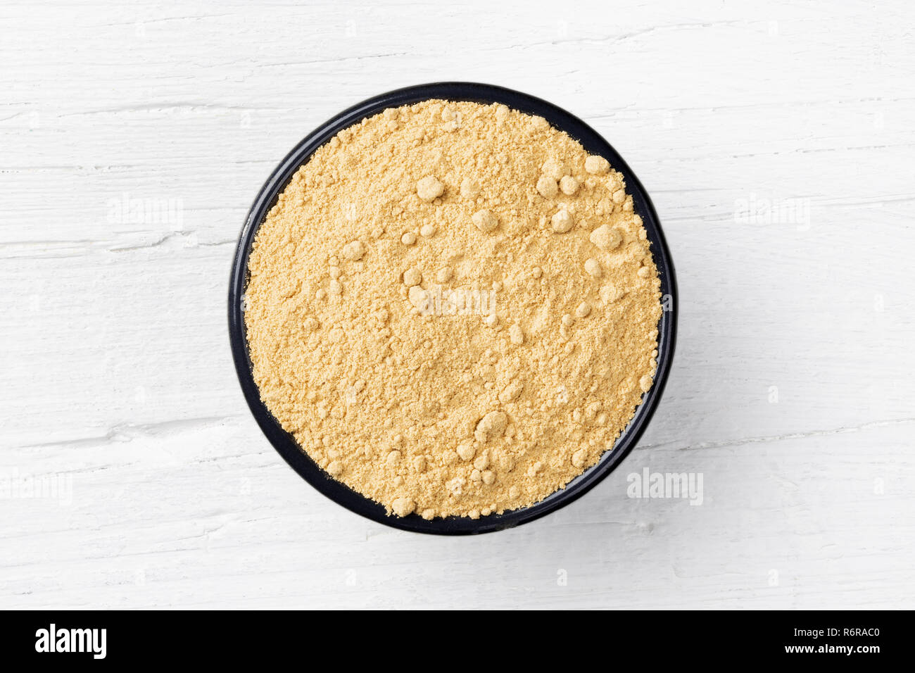Ginger powder in round cast iron bowl on white wooden background, view directly from above Stock Photo