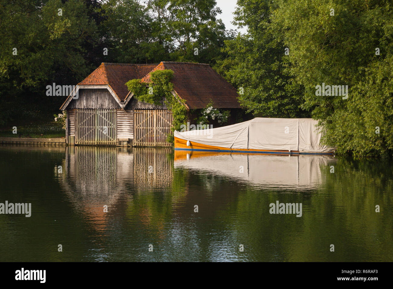 An old boathouse and classic mahogany launch under a canvas cover on the Thames at Mill End, Buckinghamshire Stock Photo