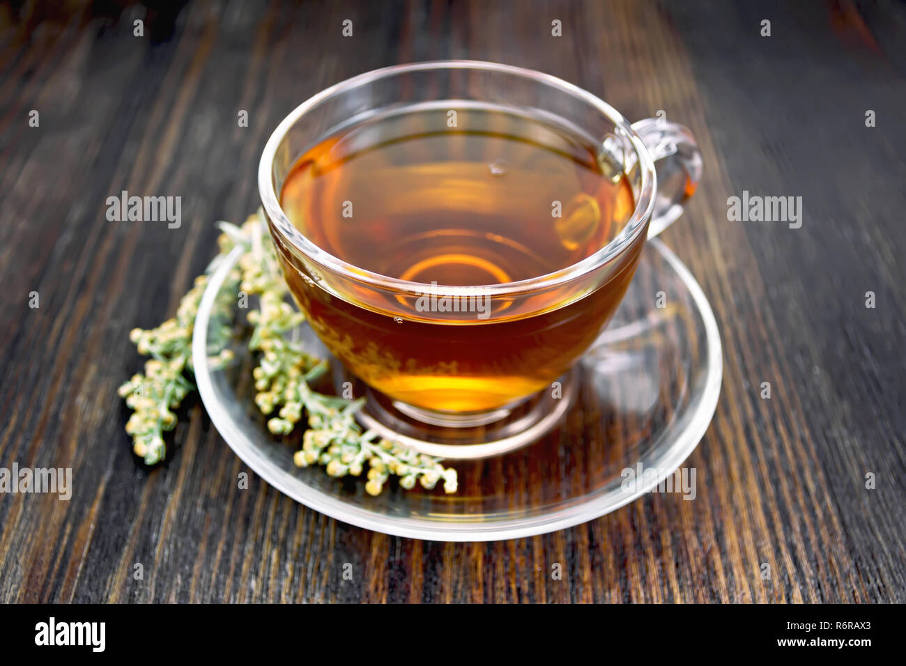 Herbal tea from wormwood in a glass cup on a saucer on a wooden boards background Stock Photo