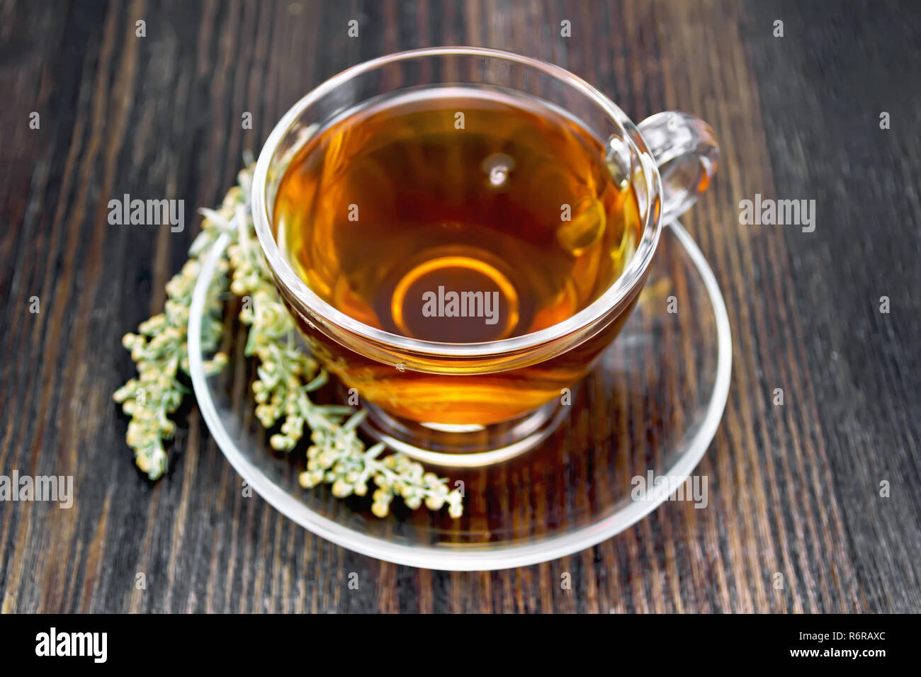 Herbal tea from wormwood in a glass cup on a saucer on a dark wooden board Stock Photo