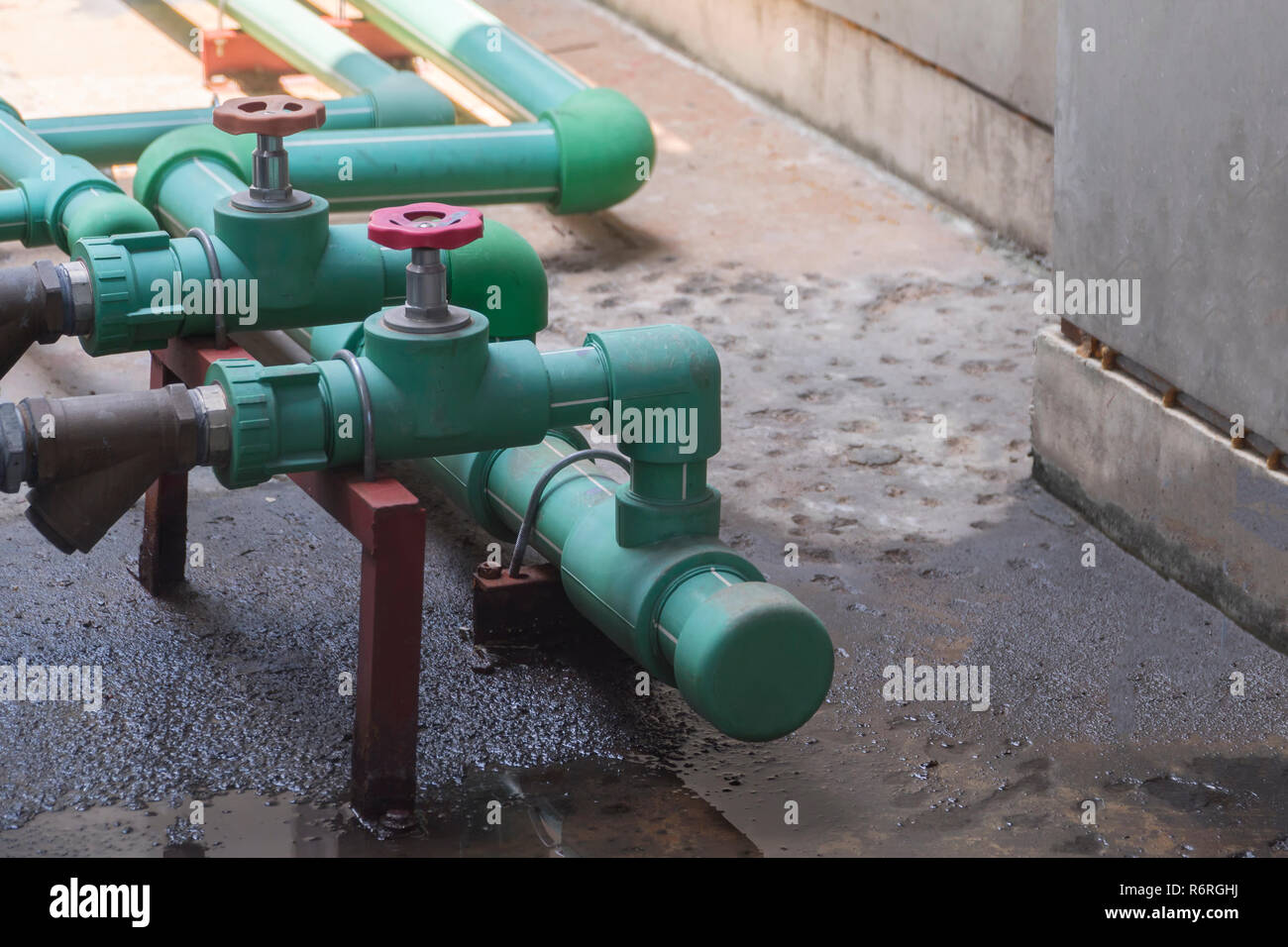 Green water pipes and water valves are on the cement floor with water