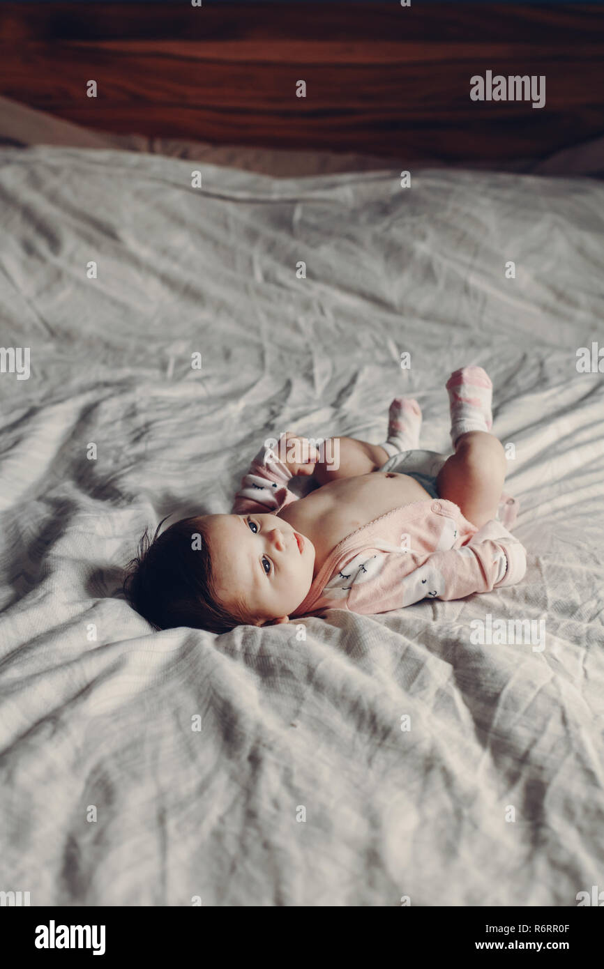 Portrait of cute adorable funny white Caucasian brunette little baby newborn wearing diaper and lying on bed in bedroom. Authentic lifestyle candid re Stock Photo