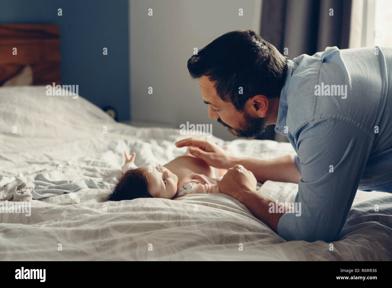 Portrait of middle age Caucasian father talking to newborn baby son daughter. Male man parent smiling to child on bed in bedroom at home. Authentic li Stock Photo