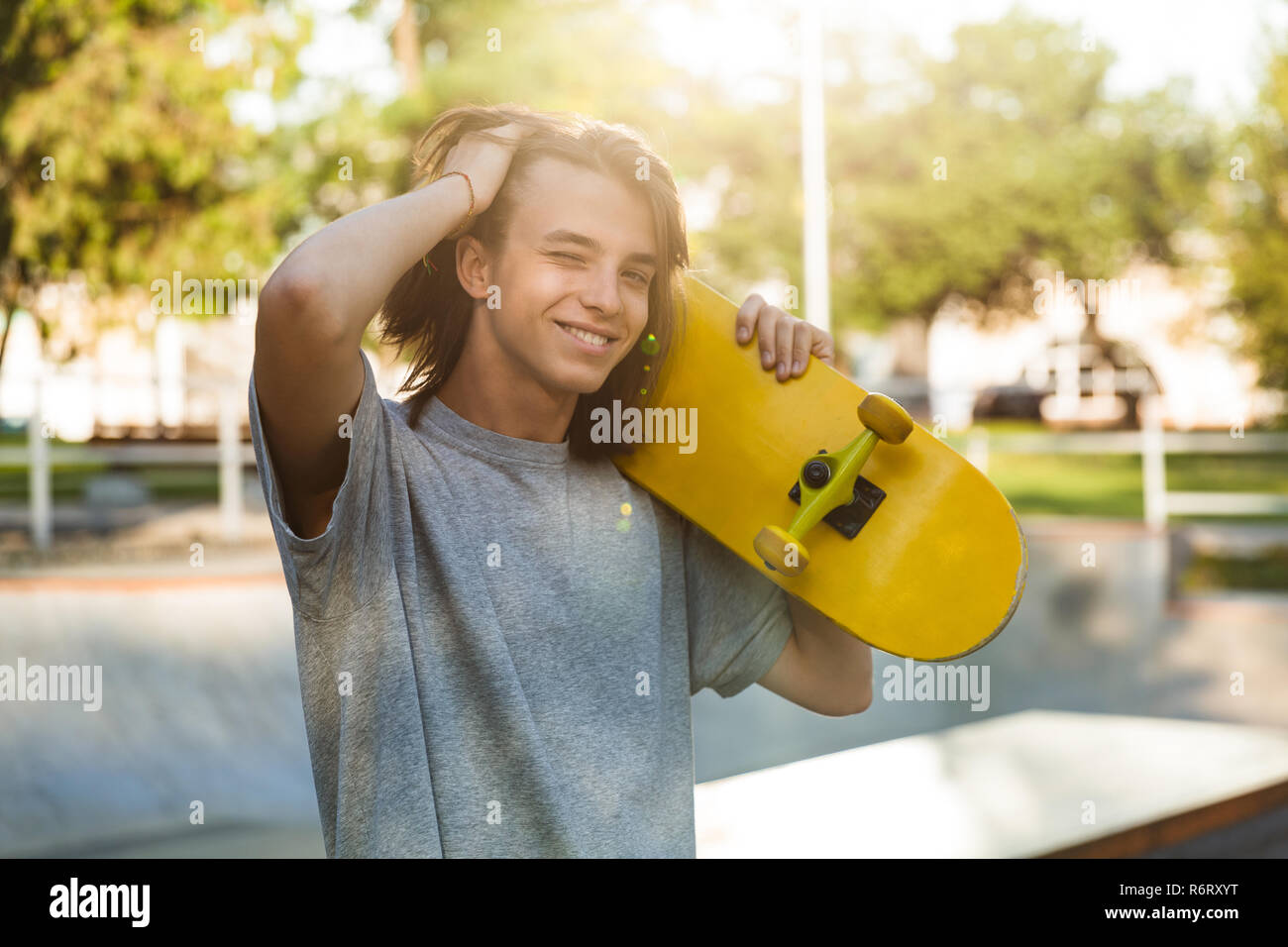 Photo of joyful skater boy 16-18 in casual wear standing with skateboard in  skate park during sunny summer day Stock Photo - Alamy