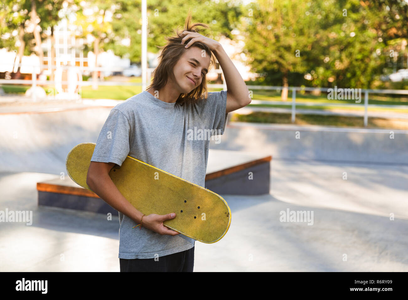 Photo of european teen guy 16-18 in casual wear standing with skateboard in  skate park during sunny summer day Stock Photo - Alamy