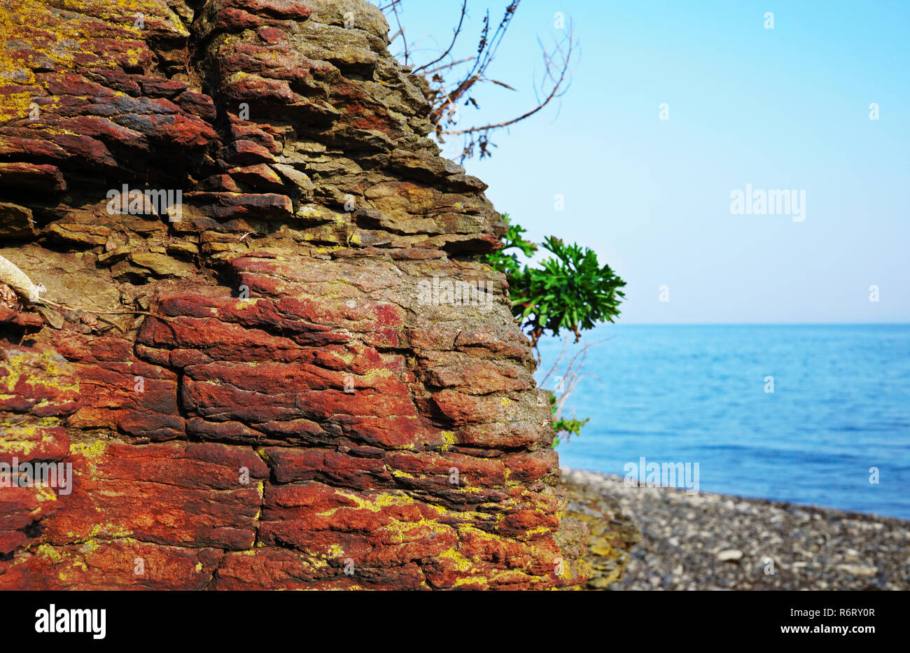 red Rock closeup against the background of the sea and pebble beach. Behind the cliffs is a seashore and blue water. East of Russia, the city of Vladi Stock Photo