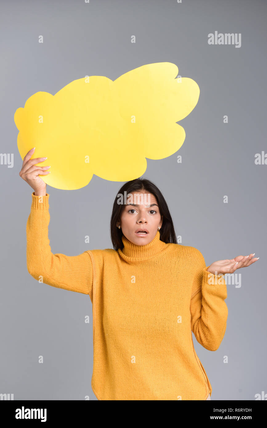 Image of a confused woman posing isolated over grey wall background holding thought bubble. Stock Photo