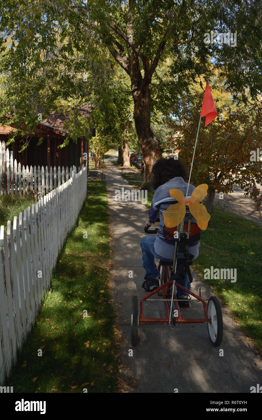 A young woman with special needs rides an adaptive bike down the sidewalk in her bike-friendly Colorado community. Stock Photo