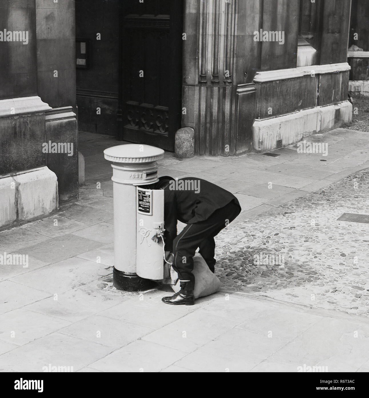 1950s, historical, a postman with his sack bending down to empty a postbox, London, England, UK. Stock Photo